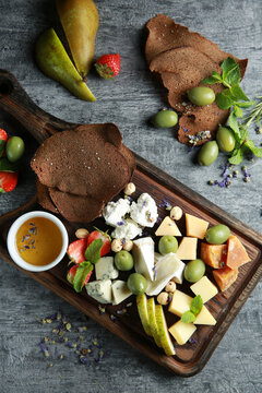 Cheese plate. Appetizer. Sliced hard cheese, cheese with mold, cheddar, camembert with olives, strawberries, pears, mint, nuts and croutons with bowl honey on dark wooden board. Background image
