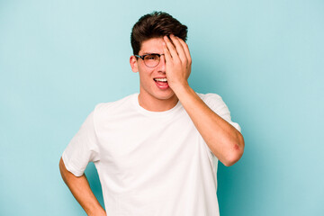 Young caucasian man isolated on blue background having fun covering half of face with palm.