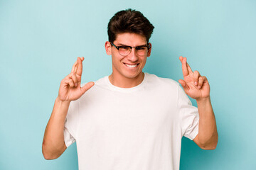Young caucasian man isolated on blue background crossing fingers for having luck