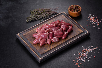 Raw uncooked chicken hearts on wooden cutting board on a dark concrete table