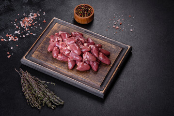 Raw uncooked chicken hearts on wooden cutting board on a dark concrete table