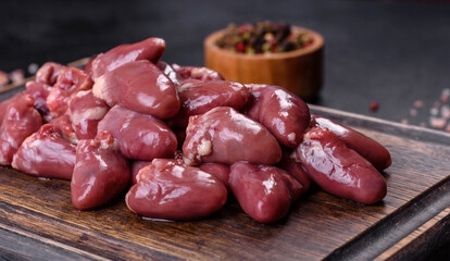 Raw uncooked chicken hearts on wooden cutting board on a dark concrete table