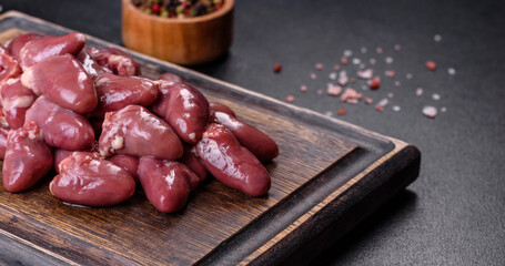 Raw uncooked chicken hearts on wooden cutting board on a dark concrete table