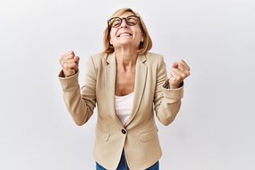 Middle age blonde business woman standing over isolated background excited for success with arms...