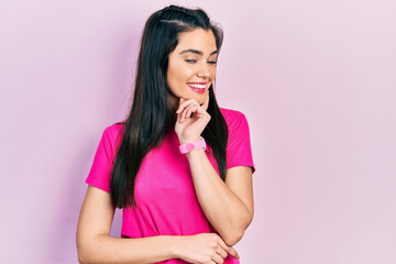Young hispanic girl wearing casual pink t shirt looking confident at the camera smiling with crossed arms and hand raised on chin. thinking positive.