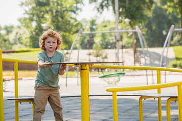 redhead boy having fun on carousel in park and looking at camera.