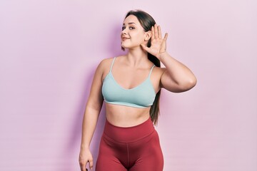 Obraz premium Young hispanic girl wearing sportswear smiling with hand over ear listening an hearing to rumor or gossip. deafness concept.