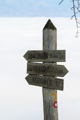 Old weathered wooden sign post with trail marking pointing to different locations on a foggy background