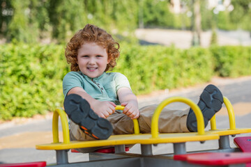 full length view of happy redhead boy riding seesaw in summer park.