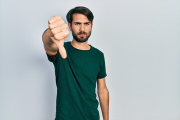 Fototapeta premium Young hispanic man wearing casual white tshirt looking unhappy and angry showing rejection and negative with thumbs down gesture. bad expression.