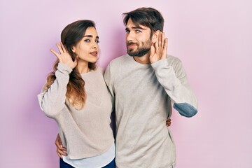 Young hispanic couple wearing casual clothes smiling with hand over ear listening an hearing to rumor or gossip. deafness concept.