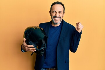 Middle age hispanic man holding motorcycle helmet screaming proud, celebrating victory and success...