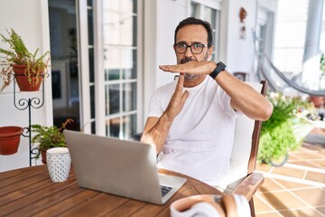 Fototapeta premium Middle age man using computer laptop at home doing time out gesture with hands, frustrated and serious face