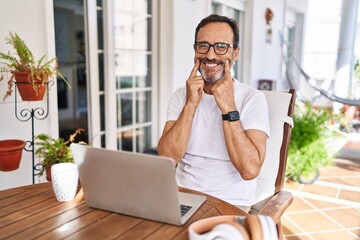 Middle age man using computer laptop at home smiling with open mouth, fingers pointing and forcing cheerful smile