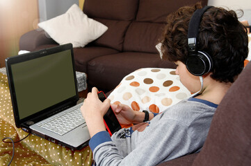 Earnest teenage boy working from a computer with headphones in his ears.