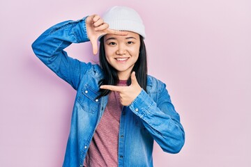 Young chinese girl wearing cute wool cap smiling making frame with hands and fingers with happy face. creativity and photography concept.