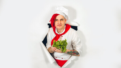 Man with red dreadlocks holds it in his hand lettuce leaves. Cook in white apron and red tie holds an ingredient for a vegetarian dish in his hand, peeking through ripped paper background