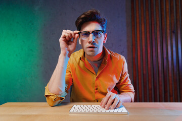 Young questioned copywriter geek software engineer IT specialist programmer man in yellow shirt glasses work at office writing code typing script on keyboard look camera Program development concept.