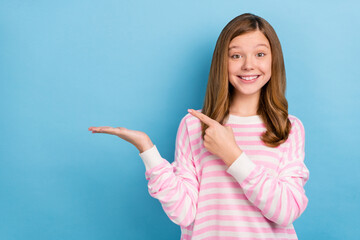 Photo of cheerful adorable girl indicate finger arm palm hold empty space isolated on blue color...