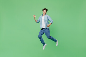 Fototapeta na wymiar Full size body length overjoyed fun excited jubilant exultant young brunet man 20s years old wears blue shirt holding hands like play guitar jumping isolated on plain green background studio portrait.