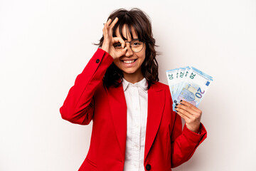 Young business hispanic woman holding banknotes isolated on white background excited keeping ok gesture on eye.