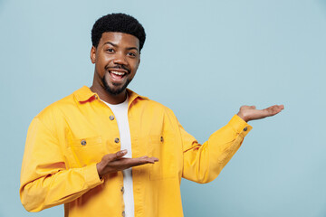 Young smiling happy man of African American ethnicity 20s wear yellow shirt point arms hands aside...