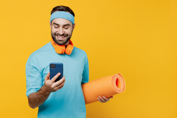 Young smiling fitness trainer instructor sporty man sportsman in headband blue t-shirt hold yoga...