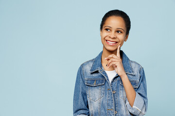 Little minded kid teen girl of African American ethnicity 12-13 years old in denim jacket prop up chin look aside on workspace area isolated on pastel plain light blue background. Childhood concept.