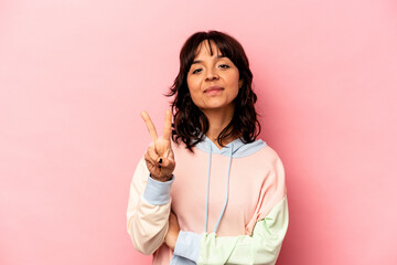 Young hispanic woman isolated on pink background showing victory sign and smiling broadly.