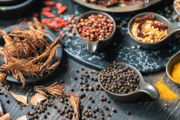 Food and Ingredent Concept. Closeup of spoon of black pepper with other spices and herbs on wooden table.