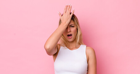 pretty blonde woman raising palm to forehead thinking oops, after making a stupid mistake or...