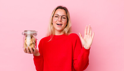 blonde pretty woman smiling happily, waving hand, welcoming and greeting you. cookies concept