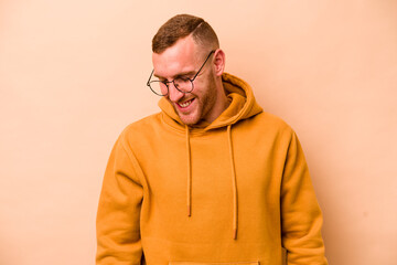 Young caucasian man isolated on beige background laughs and closes eyes, feels relaxed and happy.