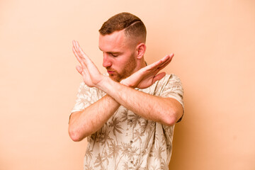 Young caucasian man isolated on beige background keeping two arms crossed, denial concept.