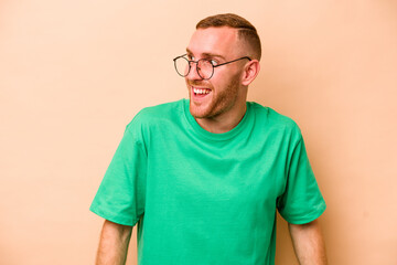 Young caucasian man isolated on beige background laughs and closes eyes, feels relaxed and happy.