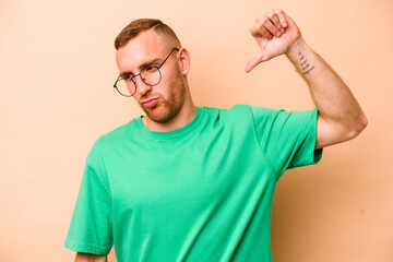 Young caucasian man isolated on beige background showing a dislike gesture, thumbs down....