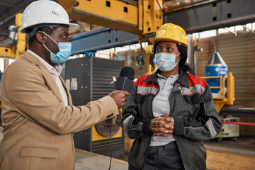 African journalist in mask interviewing the worker in uniform in factory during pandemic