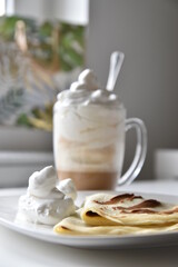 Coffee latte with frothy milk in tall glass with pancake as side dish.