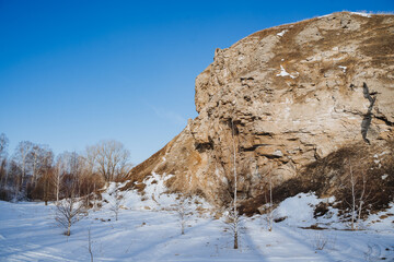 Fototapeta na wymiar The sun illuminates a large rock, a mountain against the background of a blue sky, a landscape of Natural Nature of Russia, the southern Urals of Bashkortostan, the Karlamanskaya Cave