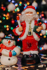 Toy Santa Claus with a bag of gifts in his hands and a snowman on the background of festive Christmas lights. Santa Claus figurine. Snowman figurine. bokeh. Christmas. New Year