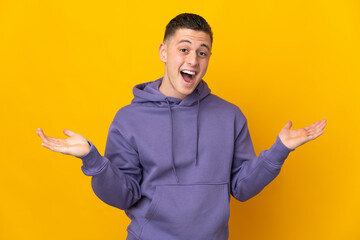 Young caucasian man isolated on yellow background with shocked facial expression