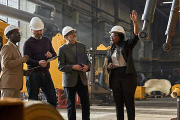 African businesswoman in work helmet presenting the new machine to business people at factory