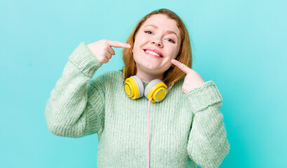 red head pretty woman smiling confidently pointing to own broad smile.  enjoying music concept