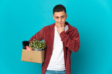 Young caucasian man making a move while picking up a box full of things isolated on blue background...