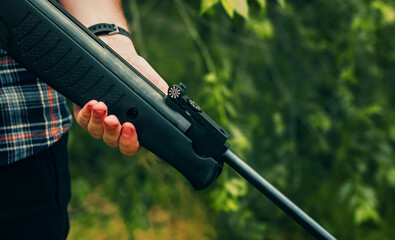 Young man with air pneumatic rifle, spring daytime, hands holding gun close up