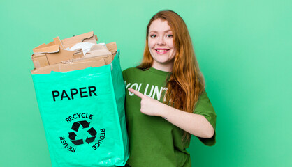 red head pretty woman smiling cheerfully, feeling happy and pointing to the side. recycling concept