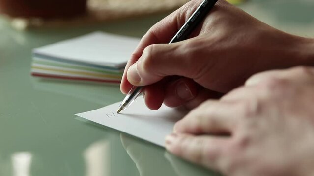 Ecrire "Hello" au stylo noir sur une feuille, un post it blanc sur une table en verre