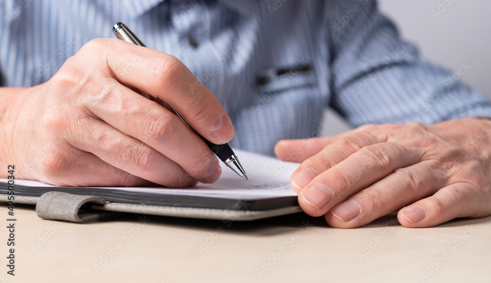 Poster Man sitting at table and writing smth in notebook. Hands closeup. Education, scheduling concept. High quality photo