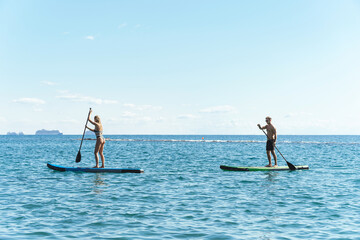 Male and female surfers riding standup paddleboards in ocean.