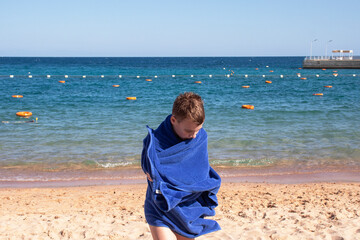 teenager boy in a blue towel on the beach